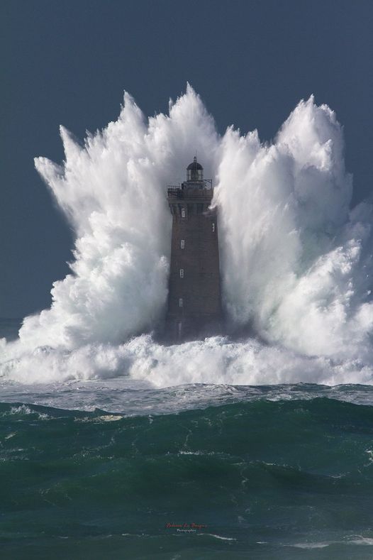 a lighthouse with a wave crashing against it.jpg